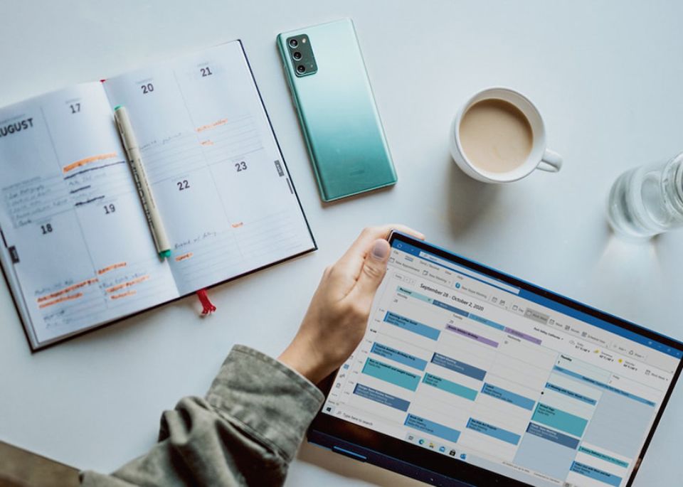 Una agenda, un móvil, un café y una tablet con una hoja de datos sobre una mesa.